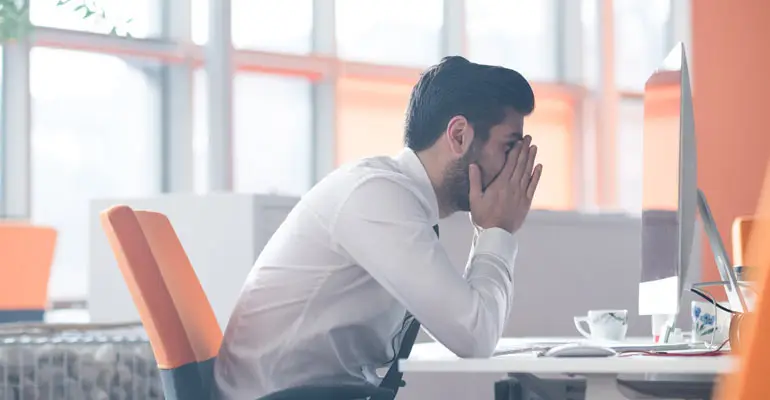 retaliation in the workplace man sitting at desk with head in hands looking at computer