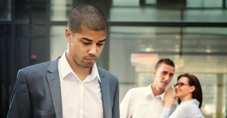 Sad man with coworkers in background talking about him