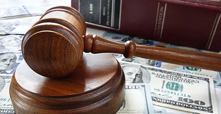 gavel atop one hundred dollar bills and law book in background